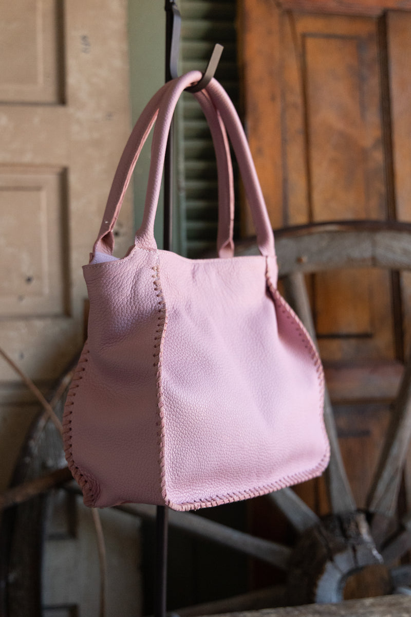 Pink leather handbag on a stand with a rustic wooden background