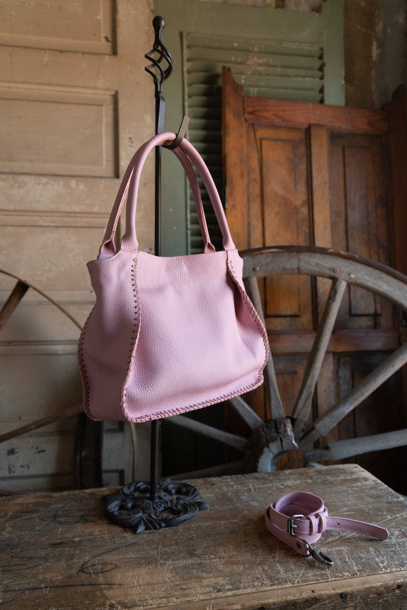 Pink handbag on a stand with a matching belt on a rustic wooden table.