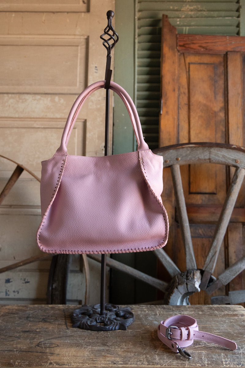 Pink handbag on a stand with a matching dog leash in front of wooden furniture.