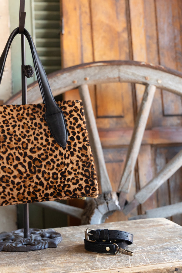 Leopard print handbag and black leather belt on a wooden surface with a rustic background