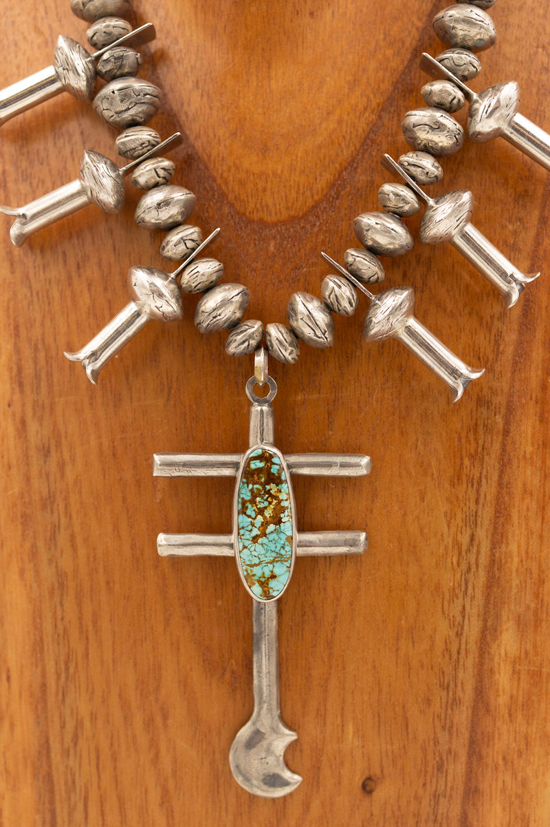 Sterling silver beaded necklace, blossoms, and center butterfly cross pendant. The center pendant also had a medium oval turquoise piece in the center. This necklace is hanging on a wooden neck display.