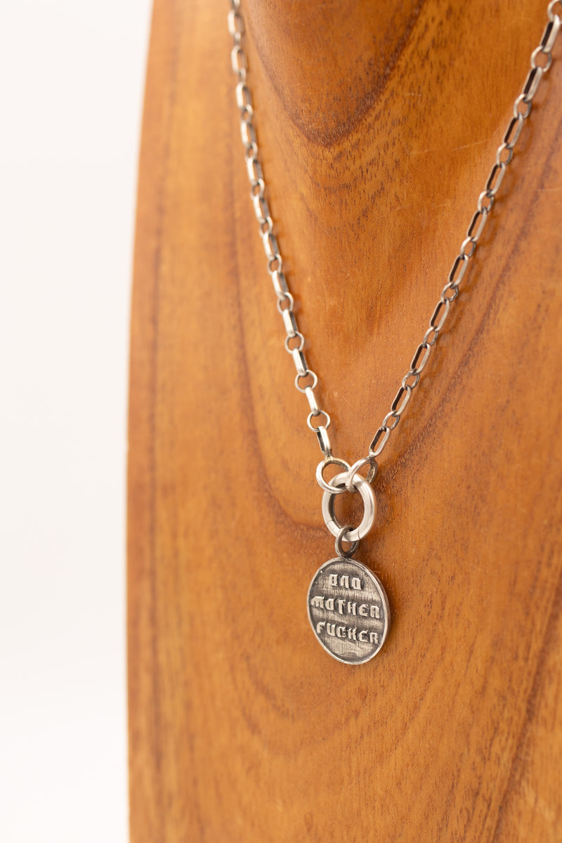 Sterling silver pendant that says "bad mother fucker" on a display necklace.