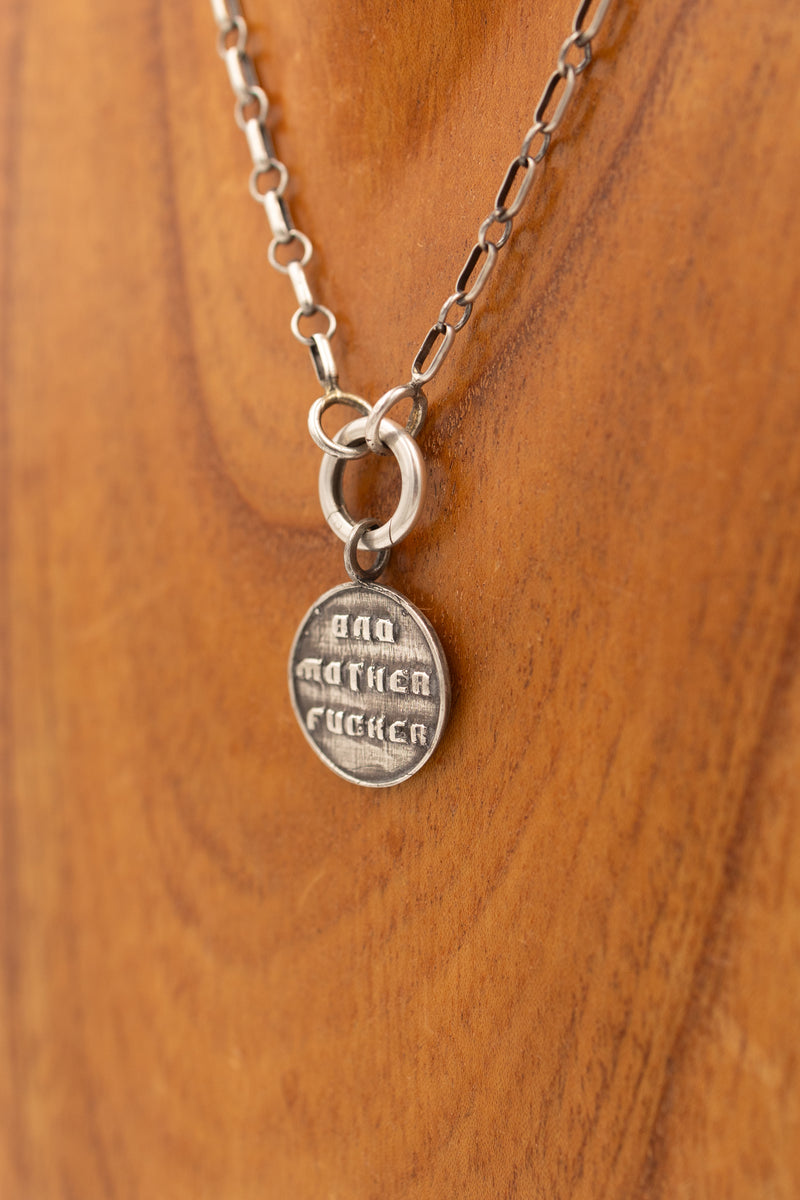 Sterling silver pendant that says "bad mother fucker" on a display necklace.