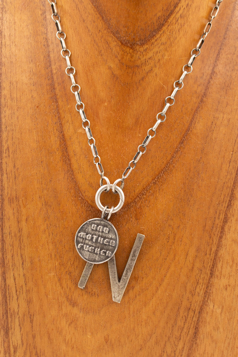 Sterling silver pendant that says "bad mother fucker" on a display necklace with other display charm.