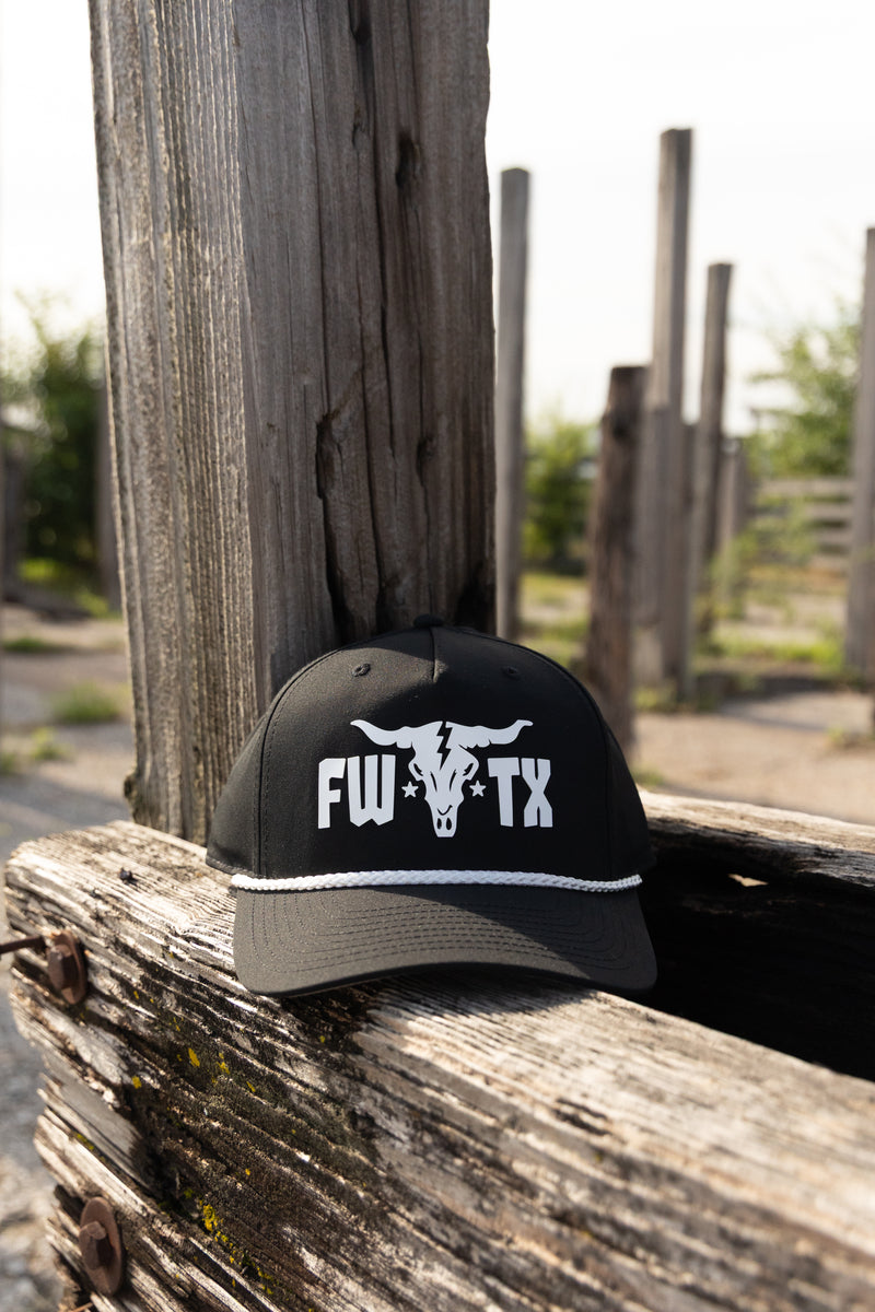 Black cap with white logo and text on a wooden post outdoors