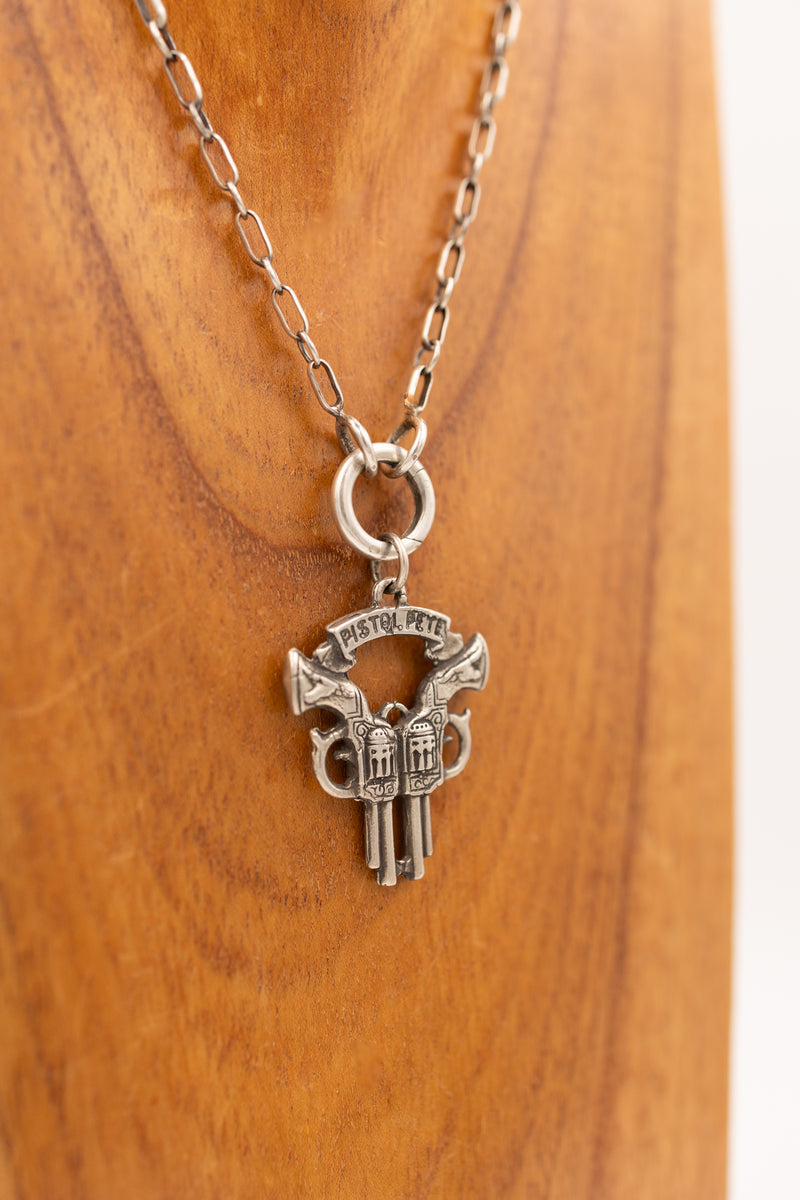 Sterling silver double gun and banner reading "pistol pete" charm on display necklace.