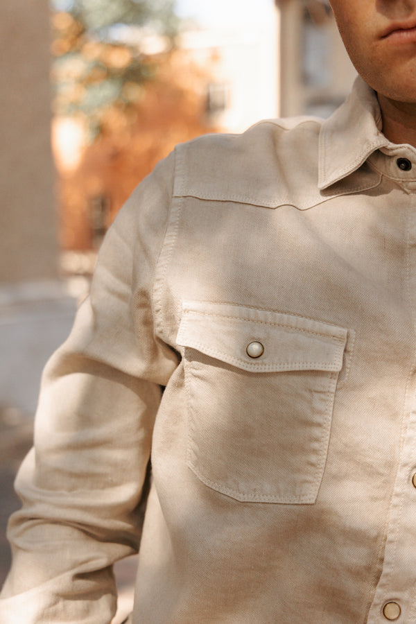 Close-up of a beige shirt with a pocket and buttons, blurred outdoor background