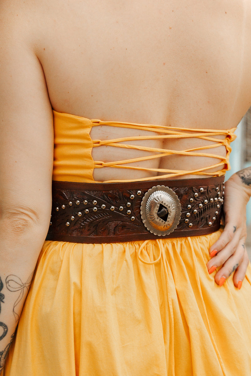 Person wearing a yellow strapless dress with a brown belt featuring a large concho.