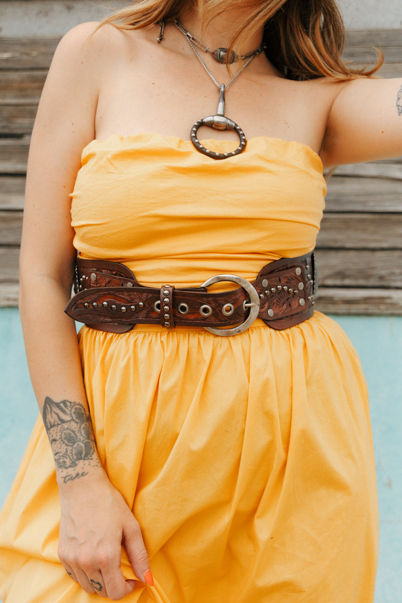 Person wearing a yellow dress with a brown belt against a wooden background