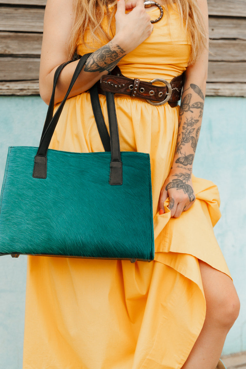 Person wearing a yellow dress holding a green and black handbag against a wooden background