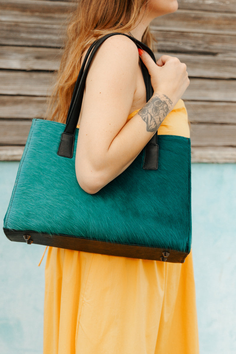Woman holding a green and black tote bag against a wooden wall.