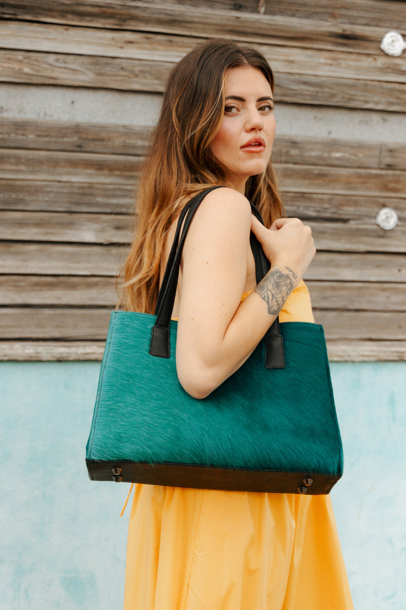 Woman holding a green tote bag against a wooden wall.