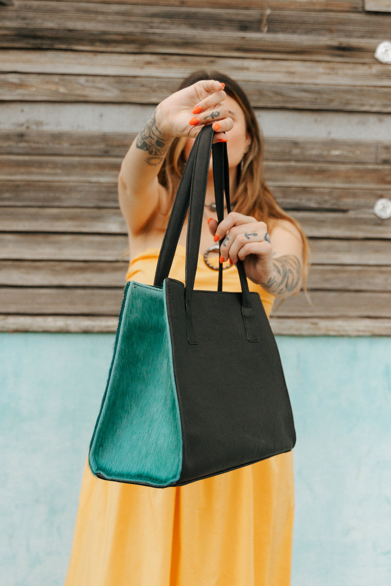 Person holding a black and green tote bag against a wooden wall.