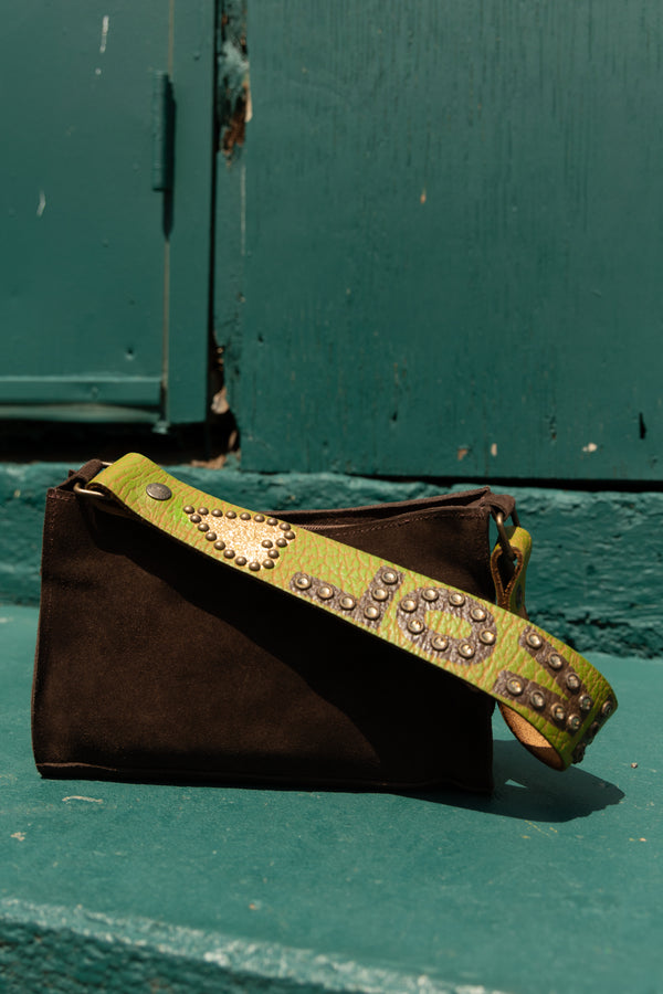 Brown handbag with a green studded strap on a teal surface