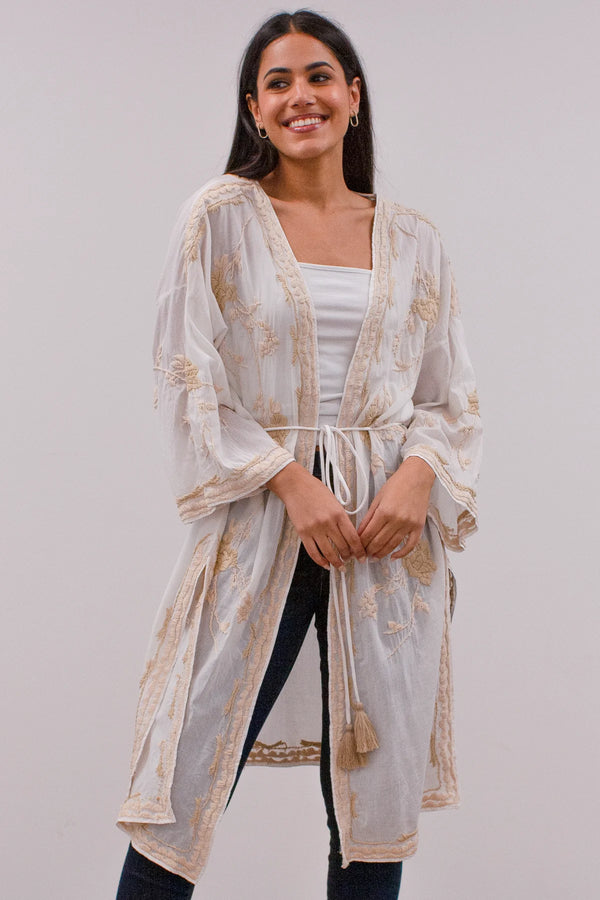Woman wearing white kimono jacket with cream embroidered floral pattern throughout