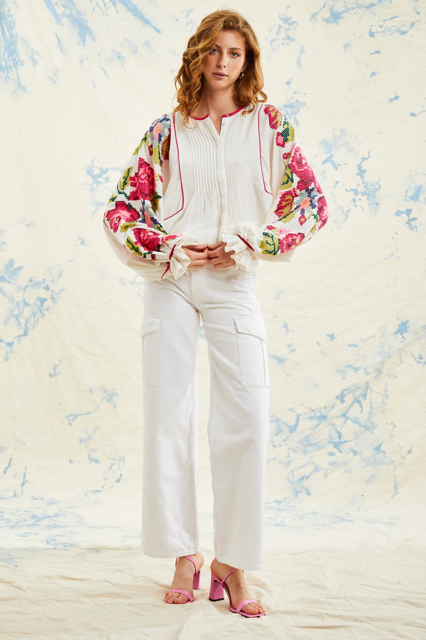 Woman wearing white blouse with long sleeves that have multicolor flowers all over them