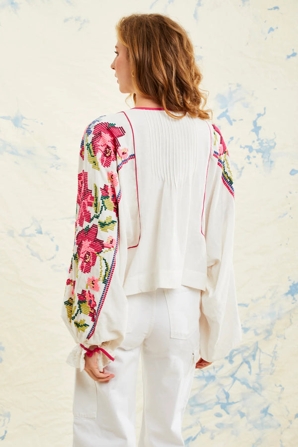 Woman wearing white blouse with long sleeves that have multicolor flowers all over them