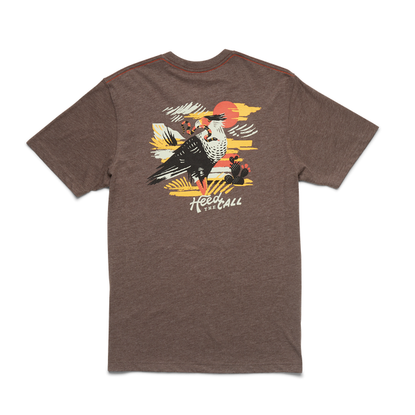 Heather brown t-shirt with graphic design on the back. Graphic design containg the image of a bird looking to its left with a snake in its mouth with the scenery of a desert in a orange, yellow, white and black color way. The bottom of the shirt contains the words "Heed the Call". 