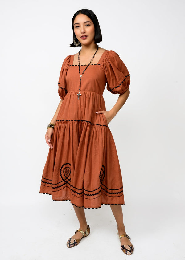 Woman wearing a brown dress with black embroidery on a white background