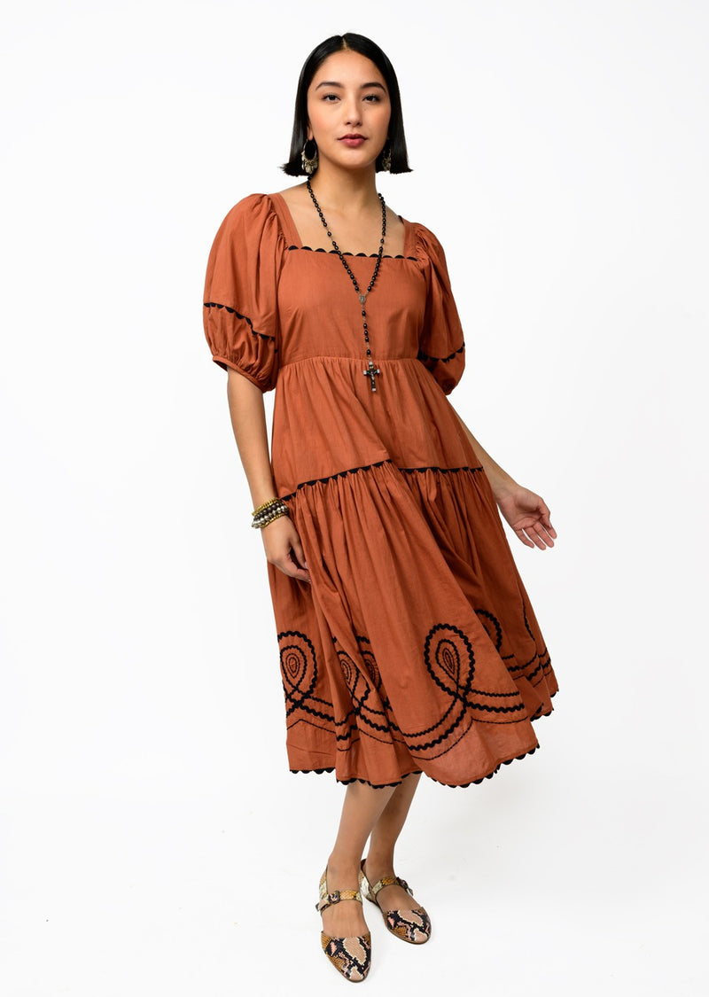 Woman wearing a rust-colored dress with black patterns on a white background