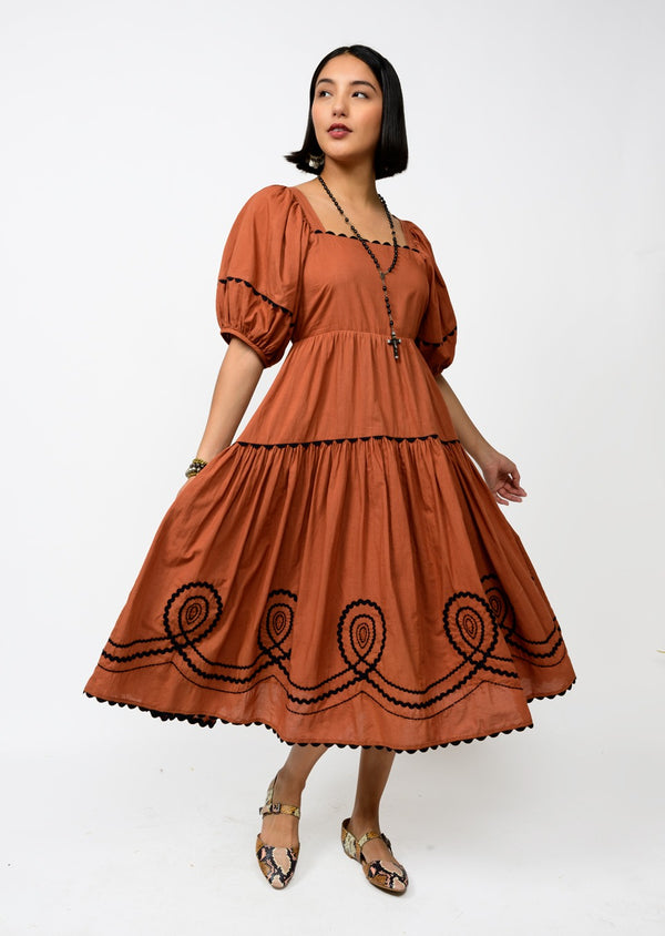 Woman wearing a rust-colored dress with black embroidery on a white background