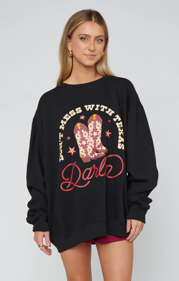 Woman wearing a black sweatshirt with cowboy boots and text design on a plain background