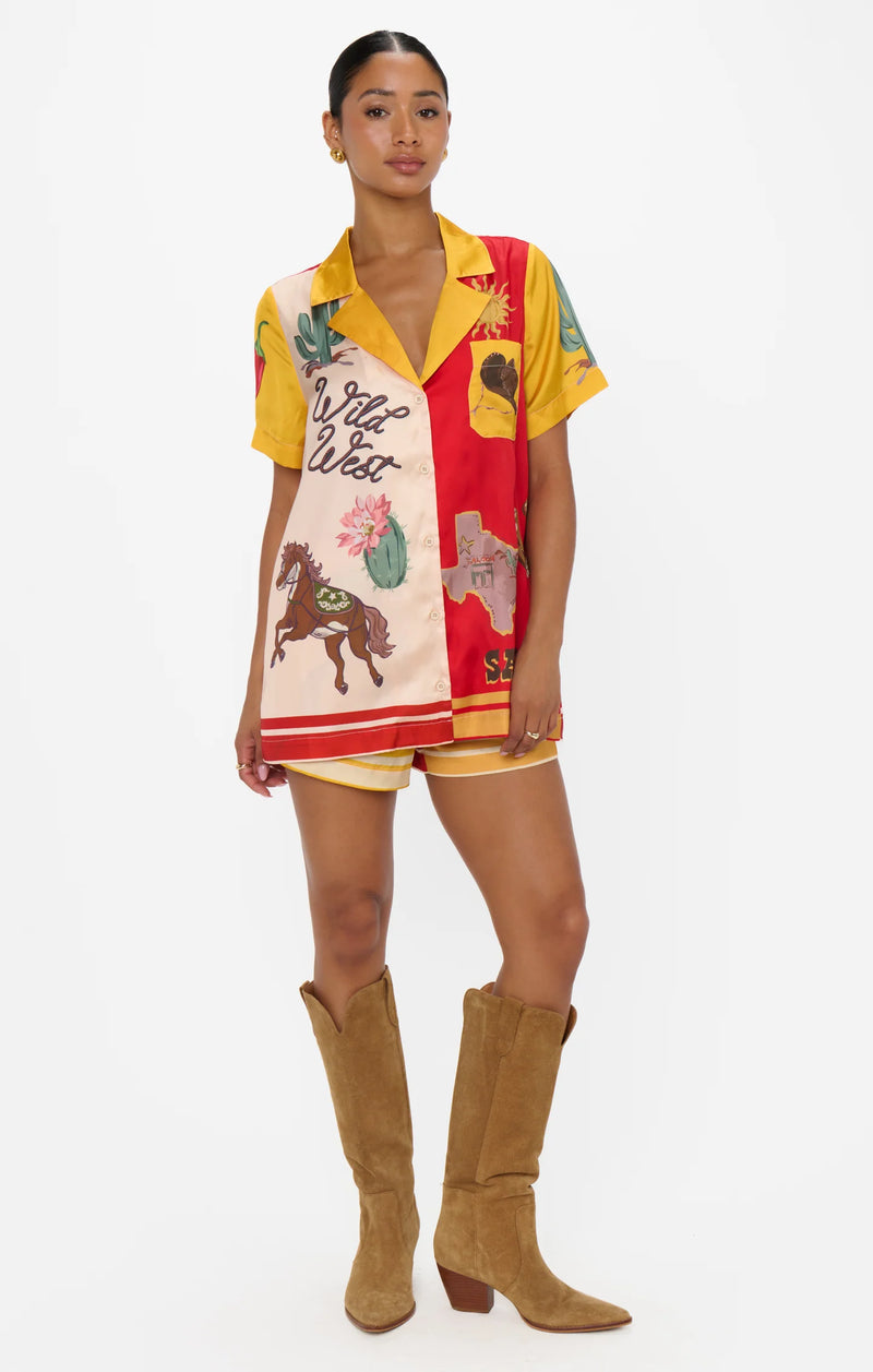 Woman wearing a colorful Western-themed shirt and boots on a white background