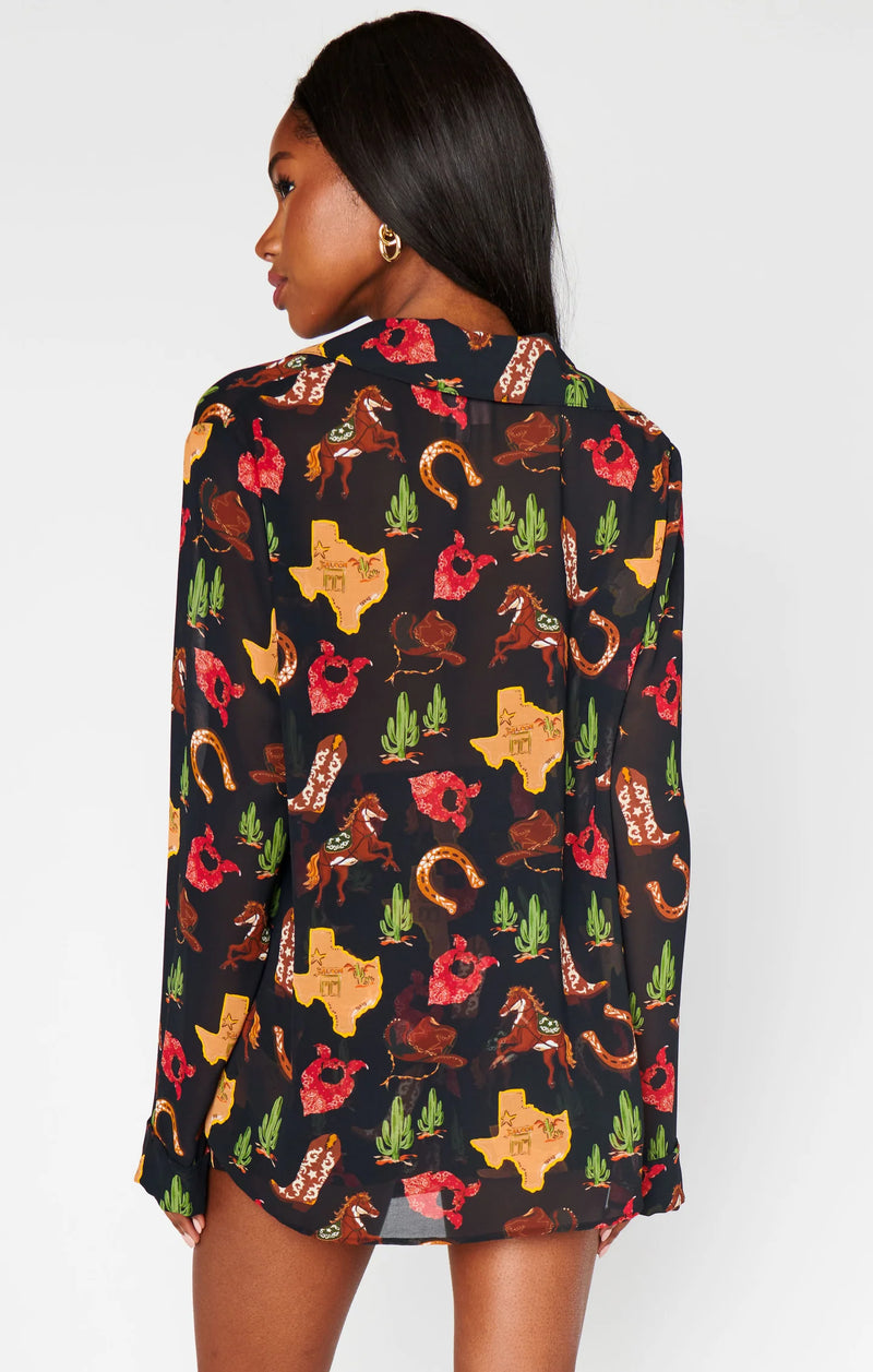 Woman wearing a long-sleeve shirt with a colorful pattern of Texas shapes, horses, and cacti on a white background.