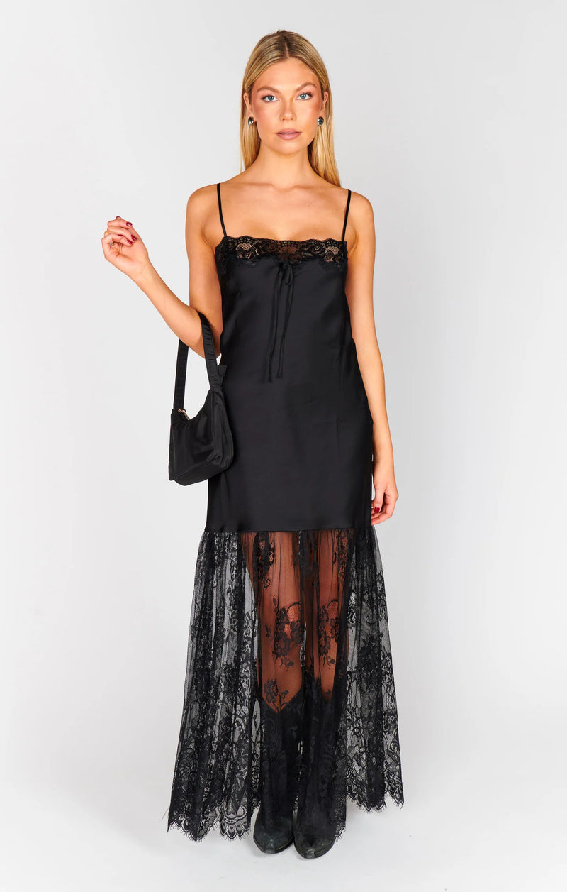 Woman wearing a black slip dress with lace detailing on a white background