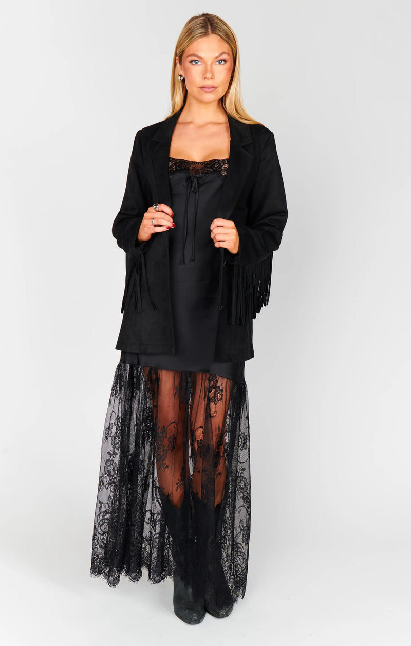 Woman wearing a black outfit with a fringed jacket and sheer skirt on a white background