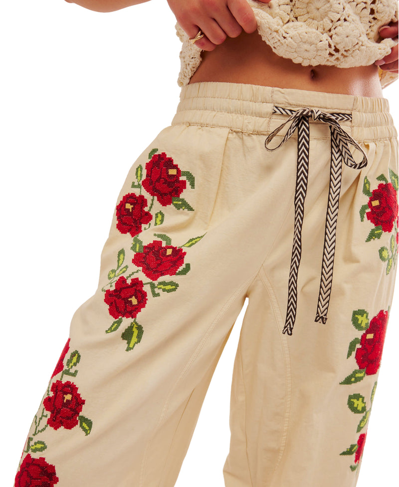 Woman wearing cream color drawstring pants with embroidered roses all over