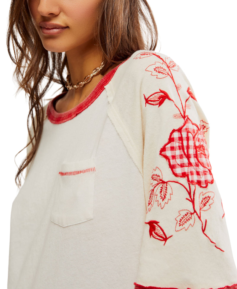 Woman wearing cream top with floral patches on the sleeves and giant number on the back