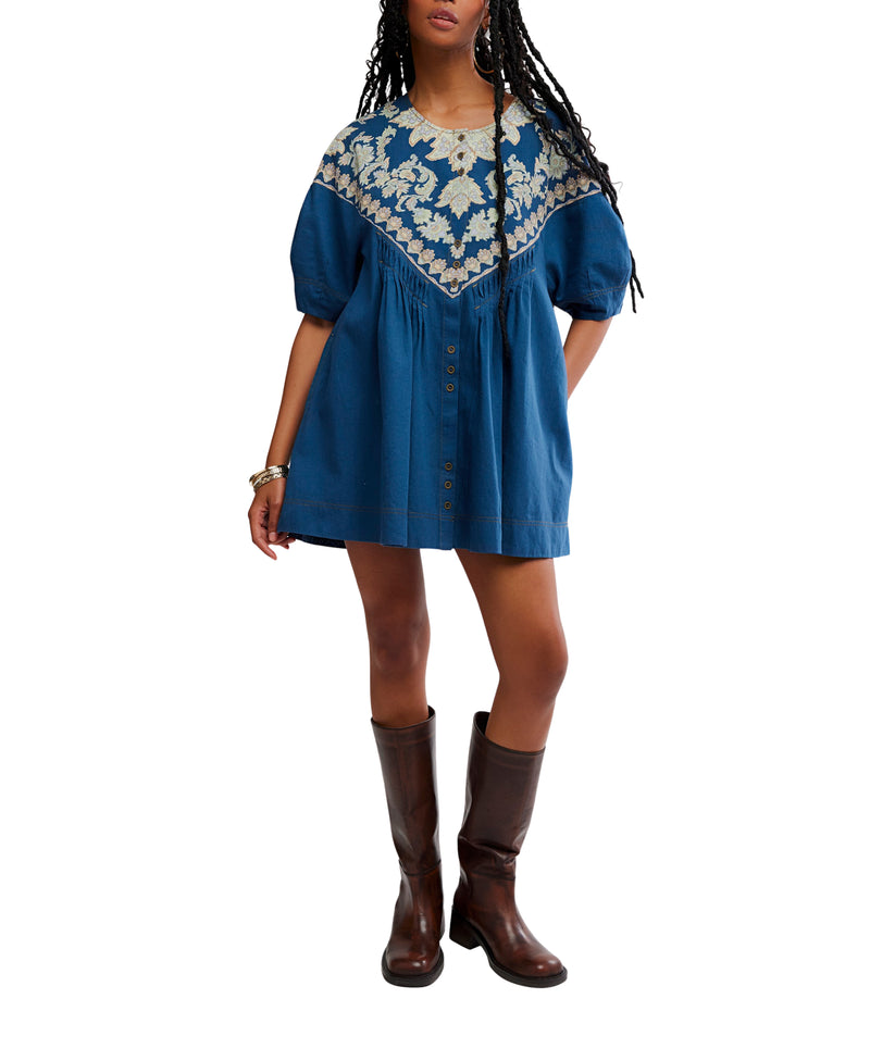 Woman wearing a blue dress with a patterned neckline and brown boots on a white background