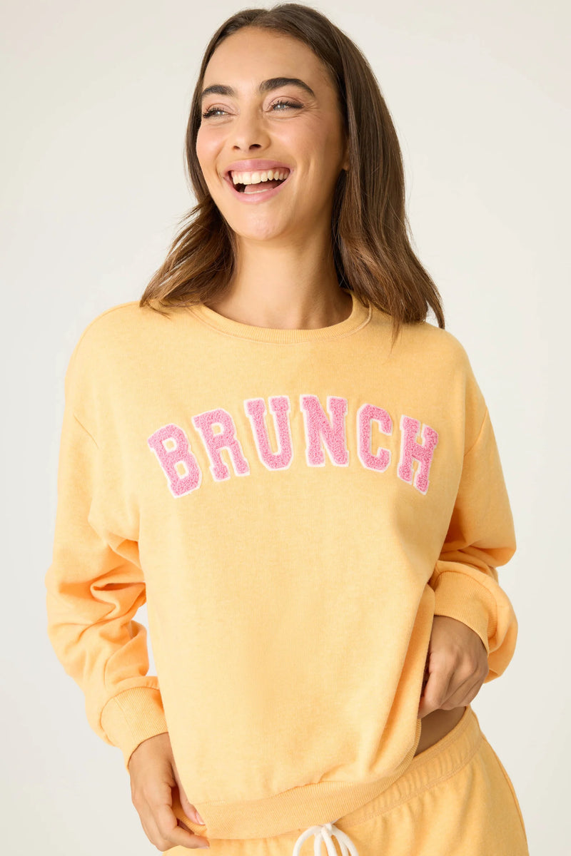 Woman wearing a yellow sweatshirt with 'BRUNCH' in pink text on a plain background