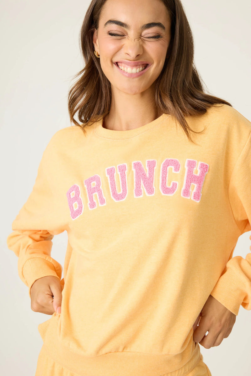 Woman wearing a peach-colored sweatshirt with 'BRUNCH' in pink text on a plain background