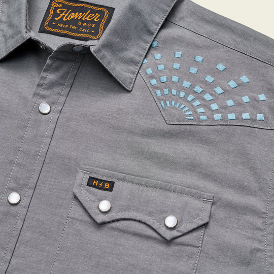 Grey short sleeve pearl snap shirt with double breast button pockets with embroidered blue square sunbeams near the shoulders