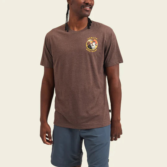 Heather brown t-shirt with graphic design on the back. Graphic design containg the image of a bird looking to its left with a snake in its mouth with the scenery of a desert in a orange, yellow, white and black color way. The bottom of the shirt contains the words "Heed the Call".