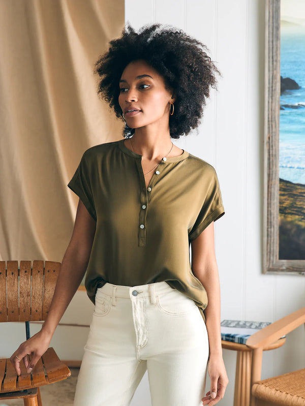 Woman wearing short sleeve blouse with buttons going half way down in an olive green color 