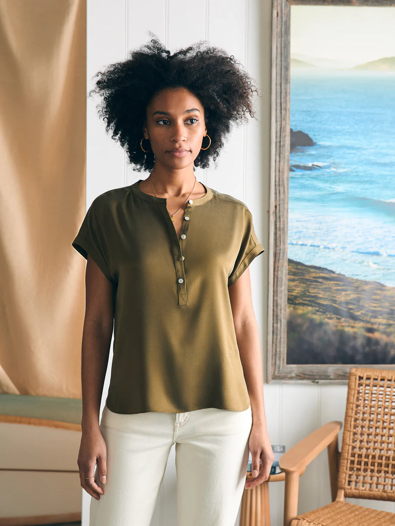 Woman wearing short sleeve blouse with buttons going half way down in an olive green color