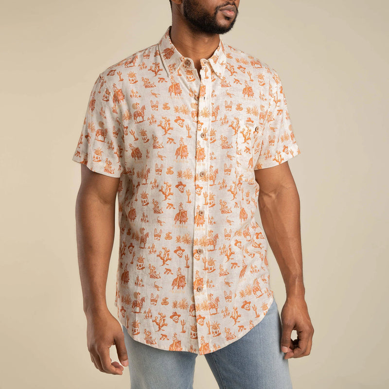 White short sleeve shirt button down with orange icons of, skull, cowboy on horse, cactus, alcohol. and agave plants repeated throughout the shirt