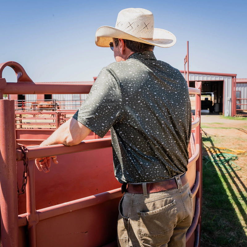 Man wearing a cowboy hat and patterned shirt standing in a red pen on a farm.
