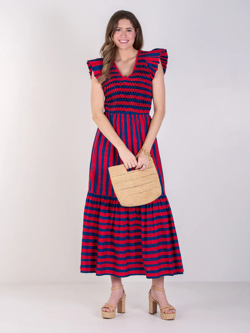 Woman wearing a red and blue striped dress holding a woven bag on a white background