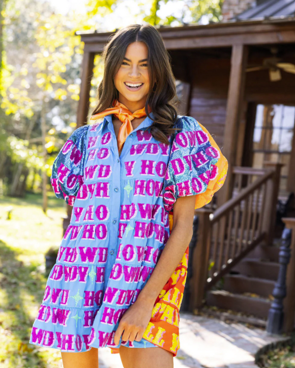Woman wearing puff sleeve tiered dress with blue fabric with sequins on the front spelling out the word "Howdy," plus orange fabric with sequins on the back reading "Yall." 