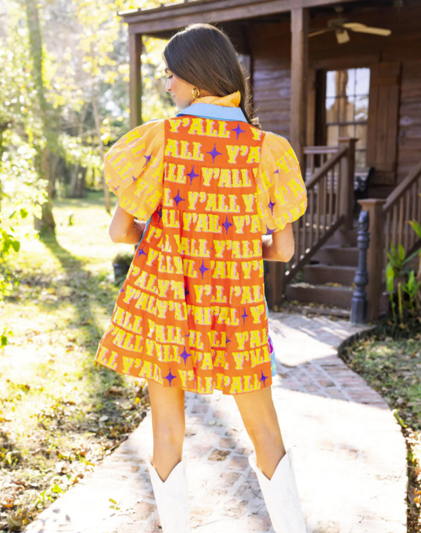 Woman wearing puff sleeve tiered dress with blue fabric with sequins on the front spelling out the word "Howdy," plus orange fabric with sequins on the back reading "Yall."