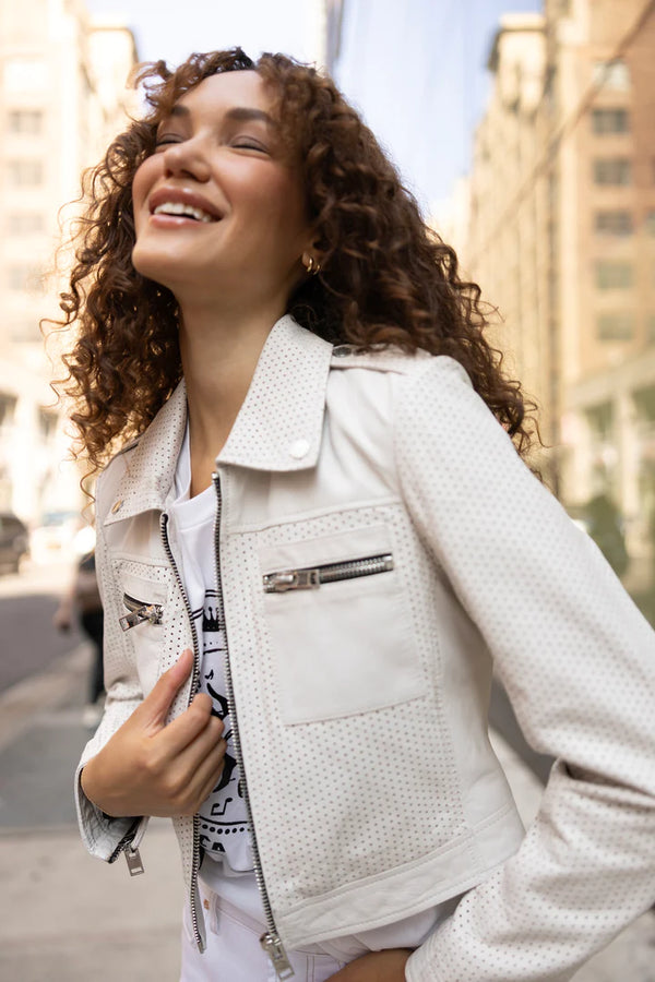 Woman wearing white leather jacket with small breathable holes throughout and double breast pockets with zippers