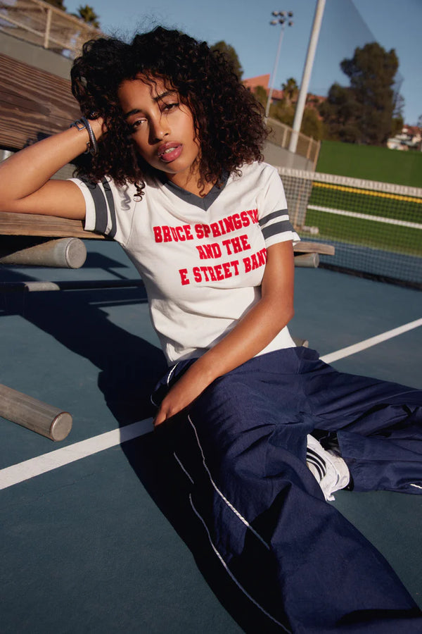 Woman wearing white tee with vintage inspiration with navy rings around the arms and red lettering spelling out "Bruce Springsteen And The E Street Band"