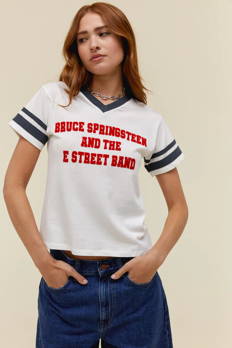 Woman wearing white tee with vintage inspiration with navy rings around the arms and red lettering spelling out "Bruce Springsteen And The E Street Band"