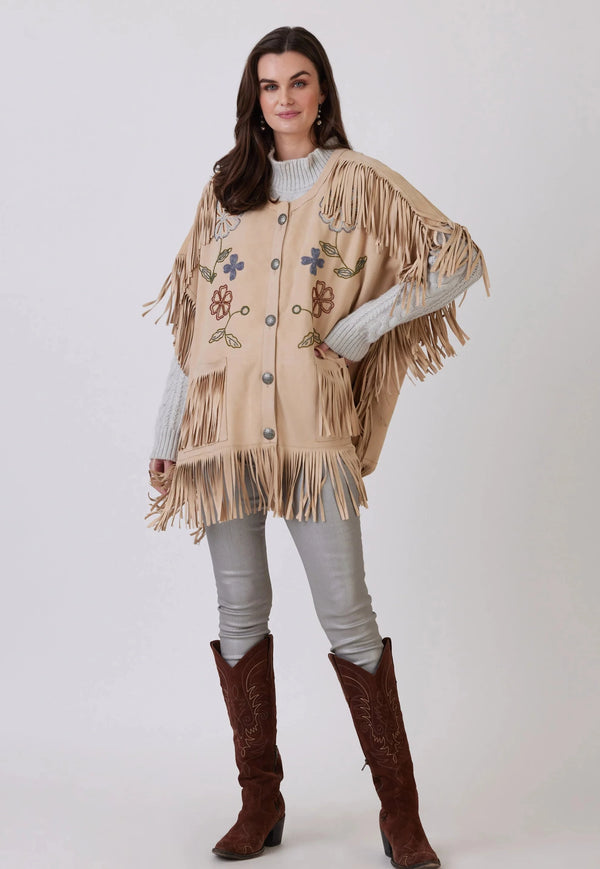 Woman wearing tan poncho with embroidered flowers and fringe accents 