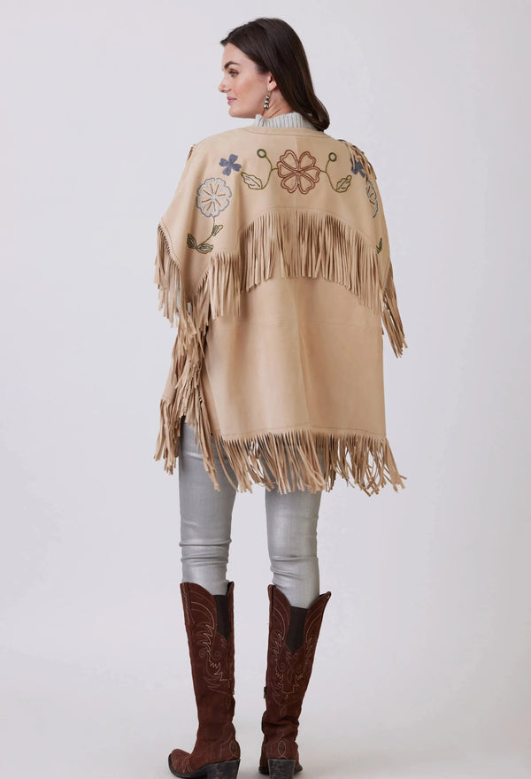 Woman wearing tan poncho with embroidered flowers and fringe accents