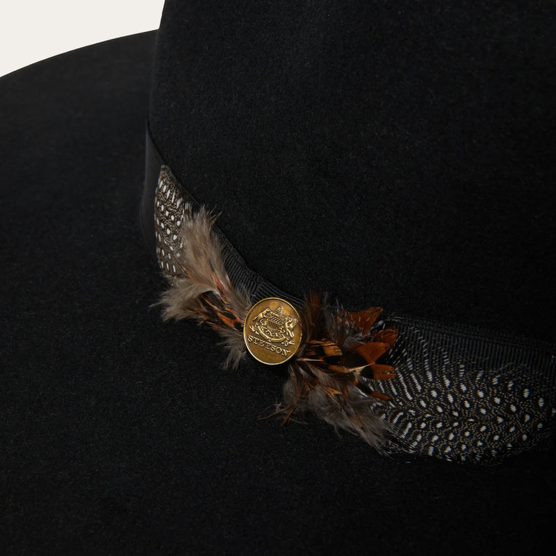 Black hat with decorative band featuring feathers and a button on a white background
